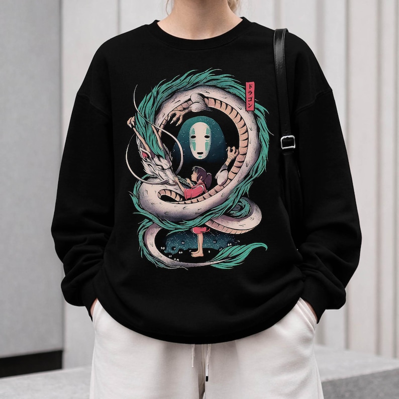 May include: Black sweatshirt featuring a detailed illustration of a white and teal dragon encircling a girl and a faceless spirit. The design includes Japanese text in a red box. The sweatshirt is worn by a person.