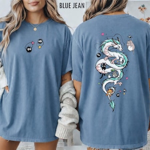 Pode incluir: Camiseta azul jeans com um gr&aacute;fico frontal de dois sprites de fuligem de desenho animado e uma estrela. A parte de tr&aacute;s da camisa apresenta um drag&atilde;o branco com detalhes verdes, cercado por personagens de desenho animado e estrelas.
