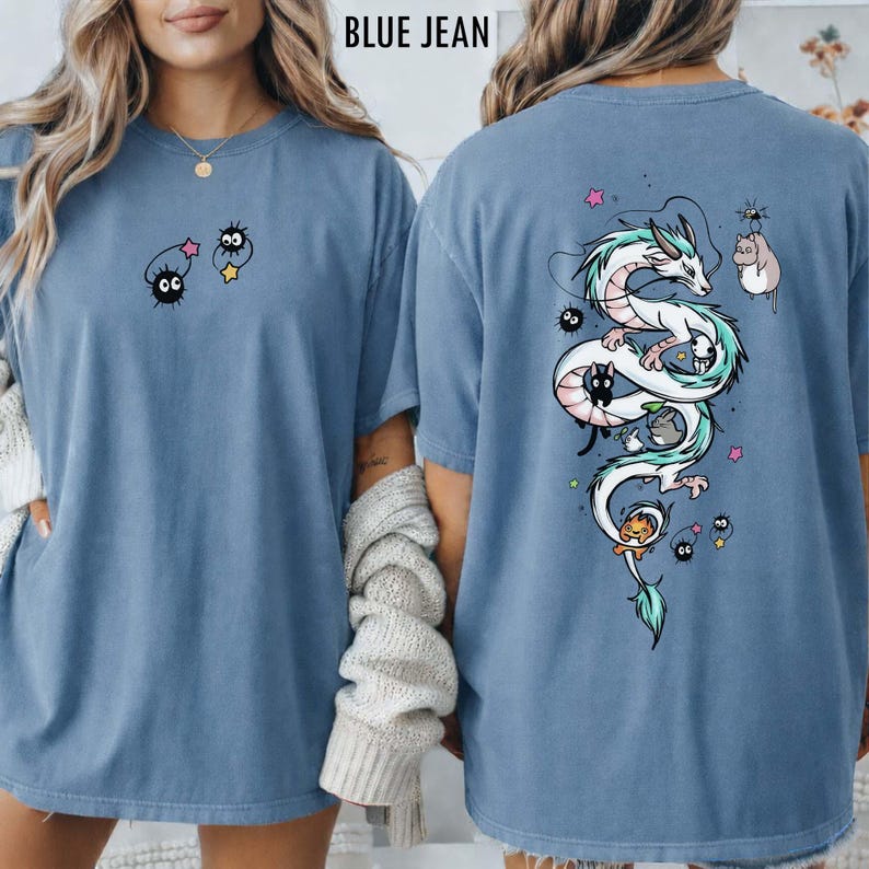 Pode incluir: Camiseta azul jeans com um gr&aacute;fico frontal de dois sprites de fuligem de desenho animado e uma estrela. A parte de tr&aacute;s da camisa apresenta um drag&atilde;o branco com detalhes verdes, cercado por personagens de desenho animado e estrelas.
