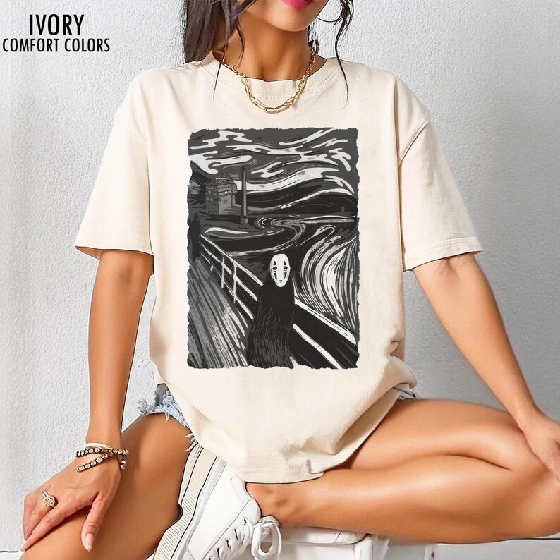 Op de afbeelding: Ivoor kleurig t-shirt met een zwart-witte grafische print. De afbeelding toont een gestileerde versie van Edvard Munchs "De Schreeuw" met een personage uit Spirited Away. De tekst "IVORY COMFORT COLORS" staat linksboven.