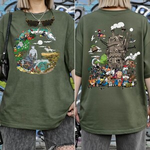 May include: Olive green t-shirt with a vibrant graphic on the front and back. The front design shows a circular landscape with fantastical creatures. The back features a detailed illustration of a castle and various characters.