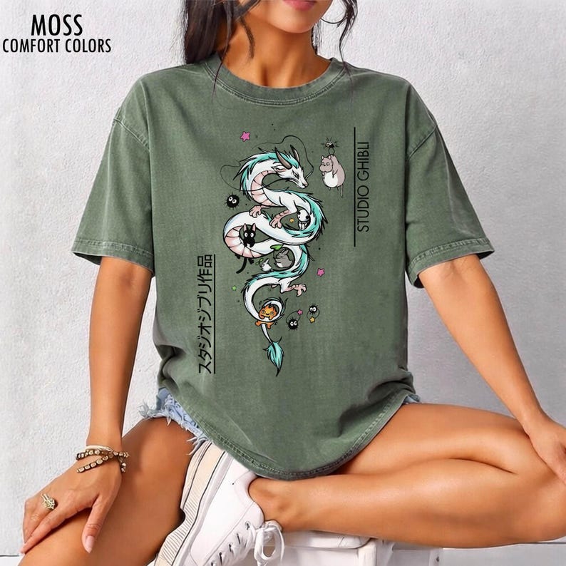 May include: Moss green t-shirt with a graphic of a white and teal dragon, black cats, and other characters. The text "STUDIO GHIBLI" and Japanese text are printed on the shirt. The shirt also has the text "MOSS COMFORT COLORS".