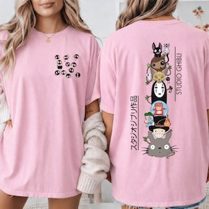 May include: Pink t-shirt featuring a small pocket design with black soot sprites. The back of the shirt displays a stacked graphic of Studio Ghibli characters with Japanese text and the Studio Ghibli logo in black.