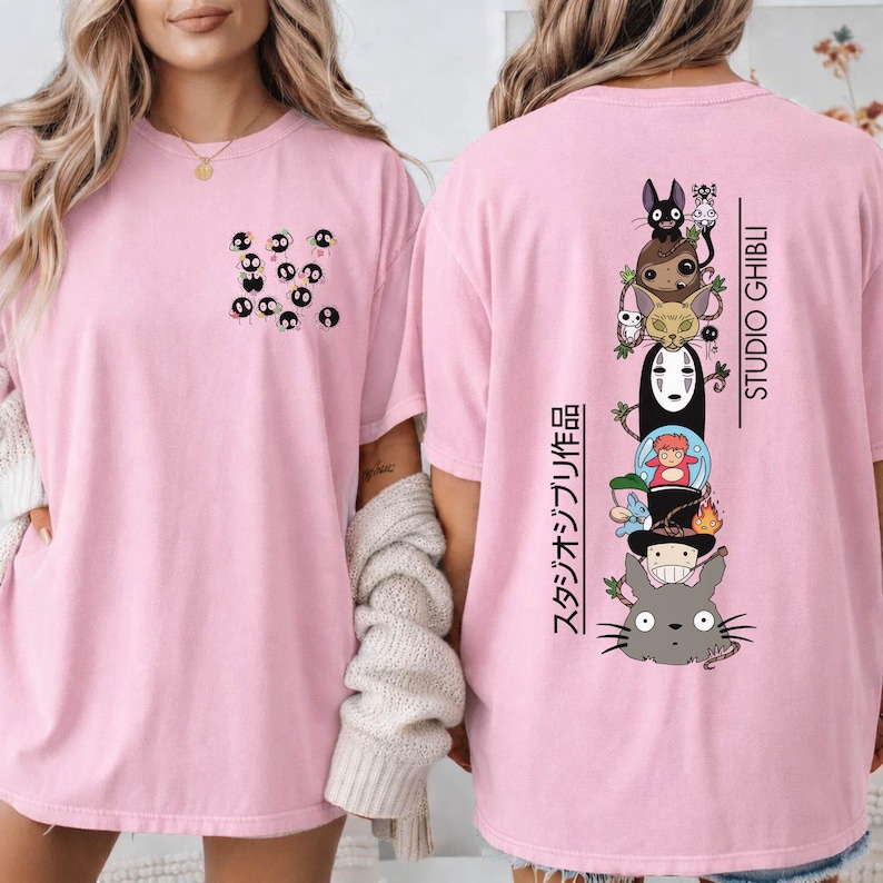 May include: Pink t-shirt featuring a small pocket design with black soot sprites. The back of the shirt displays a stacked graphic of Studio Ghibli characters with Japanese text and the Studio Ghibli logo in black.