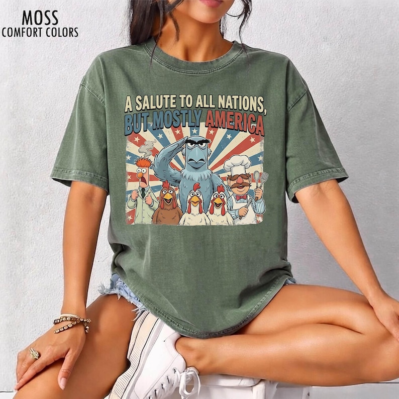 May include: Green t-shirt with the text "A Salute to All Nations, But Mostly America." The graphic features cartoon characters, including an eagle saluting, chickens, and a chef. The shirt is labeled "MOSS COMFORT COLORS."