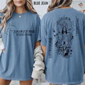 May include: Blue jean-colored t-shirt featuring a Studio Ghibli design. The front displays a Totoro graphic with Japanese text and "STUDIO GHIBLI." The back showcases a detailed illustration of characters from various Ghibli films, with Japanese text and "STUDIO GHIBLI."