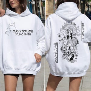 May include: White hoodie featuring a front graphic of a cartoon character and Japanese text, "スタジオジブリ作品 STUDIO GHIBLI." The back displays a detailed black and white illustration with Japanese text and "STUDIO GHIBLI."