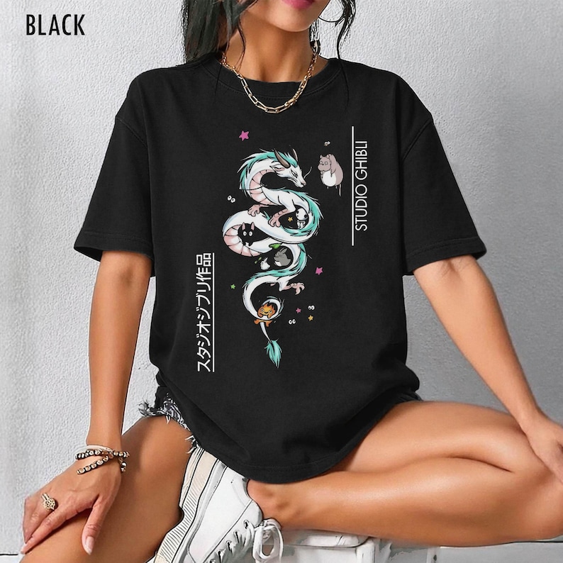 May include: Black t-shirt featuring a white and teal dragon illustration with the text "STUDIO GHIBLI" and Japanese text. The dragon design includes cartoon characters and stars. The word "BLACK" is printed at the top.