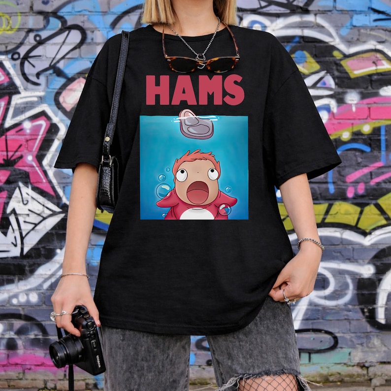 May include: Black t-shirt featuring the word "HAMS" in red above a cartoon image of a character from the animated film "Ponyo". The character is underwater, looking upwards with a surprised expression.
