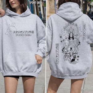 May include: Sport grey hoodie featuring a front graphic of a cartoon character and Japanese text, "スタジオジブリ作品 STUDIO GHIBLI." The back of the hoodie has a black and white illustration with Japanese text and "STUDIO GHIBLI."