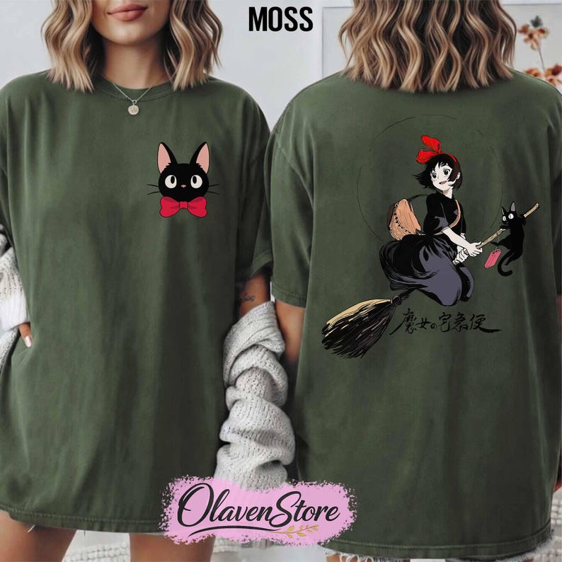 May include: Moss green t-shirt featuring a black cat with a red bow tie on the front. The back of the shirt displays a graphic of a girl on a broom with a black cat. The text "魔女の宅急便" is also on the back. The shirt has a relaxed fit.