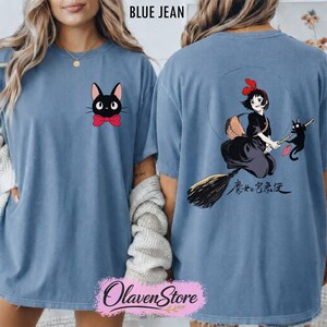 May include: Blue jean colored t-shirt featuring a black cat with a red bow tie on the front. The back of the shirt displays a graphic of a girl on a broom with a black cat and Japanese text. The text "BLUE JEAN" is at the top.