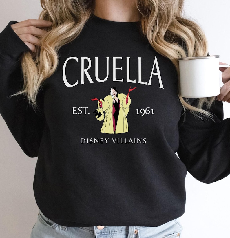 May include: Black sweatshirt with the word "CRUELLA" in white arched text above an illustration of Cruella de Vil. The text "EST. 1961" and "DISNEY VILLAINS" are also printed on the sweatshirt.