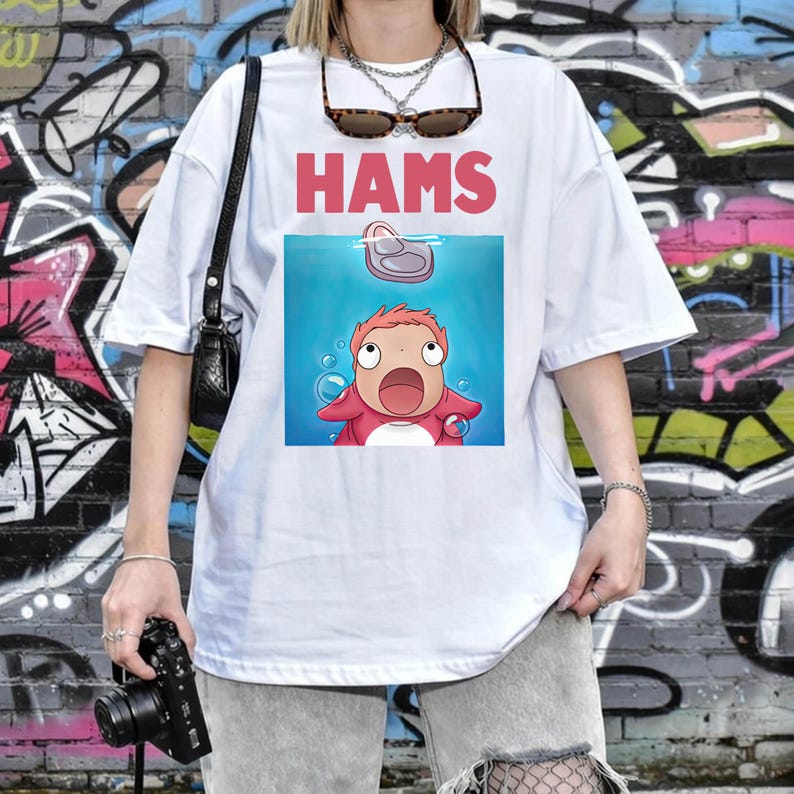 May include: White t-shirt featuring the word "HAMS" in pink above a cartoon image of a character from the animated film Ponyo. The character is in the water, looking upwards with a surprised expression.