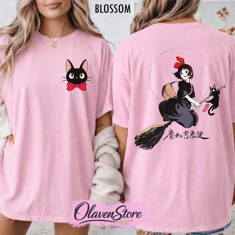 May include: Light pink t-shirt featuring a black cat with a red bow tie on the front and a graphic of a witch on a broom with a black cat on the back. The word "BLOSSOM" is printed at the top.