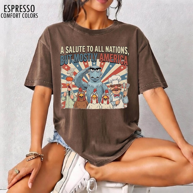 May include: Espresso-colored t-shirt with the text "A Salute to All Nations, But Mostly America." The graphic features cartoon characters including Sam Eagle, chickens, and a chef, set against a red, white, and blue background.