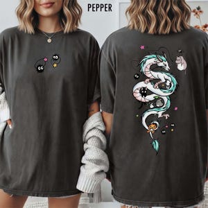 Pode incluir: T-shirt cinzenta escura com um desenho de drag&atilde;o de desenho animado nas costas e duas personagens de desenho animado na frente. O drag&atilde;o &eacute; branco com detalhes em azul e rosa. A frente da camisa tem a palavra "PEPPER".