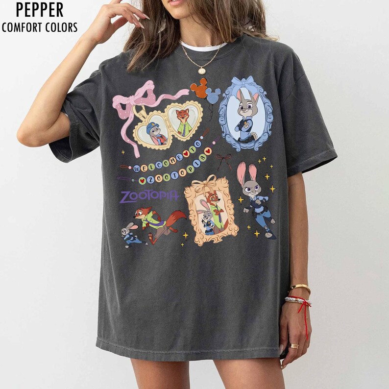 May include: A charcoal gray short-sleeve t-shirt featuring a graphic print of Zootopia characters. The design includes heart-shaped frames, a blue ornate frame, and the text Welcome to Zootopia. The shirt has a relaxed fit and crew neckline.