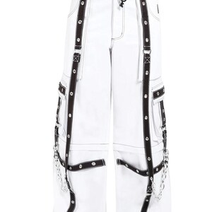 May include: White cargo pants with black straps and silver chains. The pants have multiple pockets and a drawstring waist.