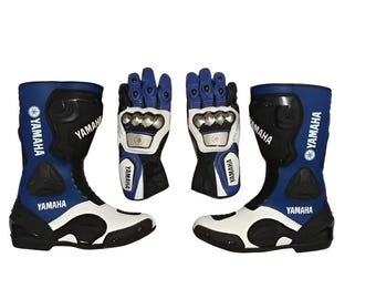 May include: A pair of blue, black, and white Yamaha motorcycle boots and gloves. The boots have Yamaha branding and a white sole. The gloves are black and white with blue accents and silver knuckle protectors. The set is designed for motorcycle riding.