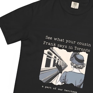 May include: Black t-shirt with a graphic featuring a vintage illustration of a woman in a hat and gloves, with a train in the background. Text reads "See what your cousin Frank says in Toronto" and "a part of our heritage."
