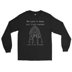 Peut inclure: T-shirt noir à manches longues avec le texte "We have to keep our Irish names" au-dessus d'un dessin de trois personnages devant un vitrail. Le texte "a part of our heritage" est en dessous.