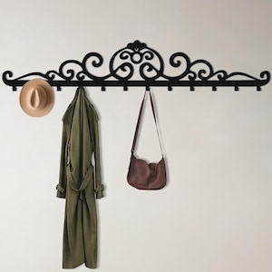 May include: Black metal wall-mounted coat rack with a decorative scrollwork design. A tan hat, olive green coat, and brown purse hang from the hooks. A potted plant sits to the right, with a light wood floor.