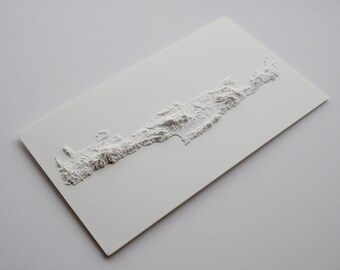 May include: A white relief map of an island, possibly Crete, showing detailed topographical features. The raised surface depicts the island's shape and elevation, creating a 3D effect. The map is mounted on a white rectangular base.
