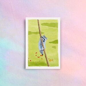 May include: Watercolour painting of a raccoon clinging to a rope. The raccoon is grey and white, with a black mask. The background is a light green with some orange and brown details. The artwork is on a white rectangular paper.