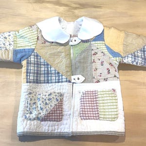 May include: A patchwork jacket with a white collar and two front pockets. The jacket is made of various fabric patterns, including floral, plaid, and solid colors. The jacket is a mix of blue, green, red, and tan colors.