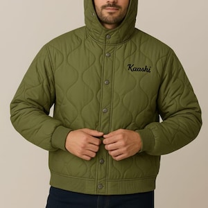 Op de afbeelding: Olijfgroene gewatteerde bomberjack met capuchon en knoopsluiting. De jas heeft het geborduurde woord "Kaashi" en maakt deel uit van een digitaal PDF naaipatroon. Inclusief maten van XXS tot 5XL.