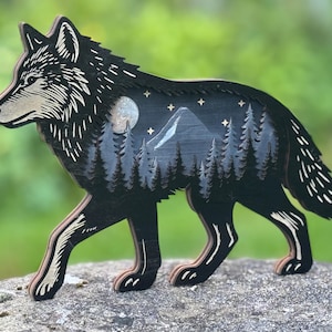 May include: A wooden wolf figurine with a detailed design. The wolf is black with a light beige snout and paws. The interior features a mountain scene with trees, a moon, and stars. The figurine is approximately 10 inches long.