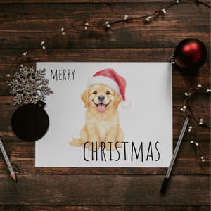 May include: A Christmas card with a smiling golden retriever puppy wearing a Santa hat. The words "MERRY CHRISTMAS" are printed above and below the dog illustration. The card is on a wooden surface with decorative elements.