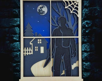 May include: Wooden layered art piece depicting a spooky scene through a window. The artwork features a silhouette of a figure holding a knife, a house, a full moon, and a spiderweb. The color palette includes blue, black, and natural wood tones.