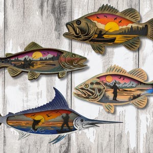 May include: Four wooden fish-shaped wall art pieces. Each fish features a layered design with a sunset scene, including a fisherman, boat, or jumping fish. The colour palette includes shades of brown, orange, and blue.