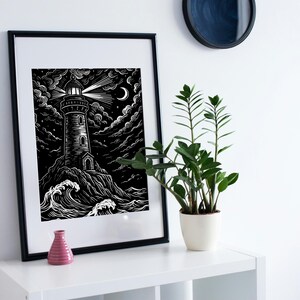 May include: Black and white framed art print of a lighthouse on a rocky shore under a night sky with clouds, a crescent moon, and stars. The lighthouse beam shines brightly. A small pink vase and a potted plant are on a white shelf.