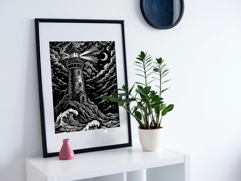 May include: Black and white framed art print of a lighthouse on a rocky shore under a night sky with clouds, a crescent moon, and stars. The lighthouse beam shines brightly. A small pink vase and a potted plant are on a white shelf.