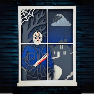May include: A multi-layered wooden art piece depicting a scene through a window. The artwork features a figure in a hockey mask holding a bloody machete, a spider web, a tree, a full moon, and a house. The color palette includes blue, gray, white, and red.