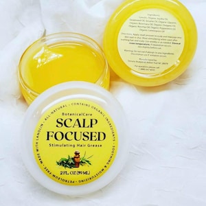 May include: A white jar with a yellow lid containing a yellow hair grease. The jar is labelled "BotanicalCare Scalp Focused Stimulating Hair Grease 2 fl oz (59 ml)". The label also states "Made with Lanolin All Natural Contains Organic Ingredients Soothing & Moisturizing Petroleum-Free".