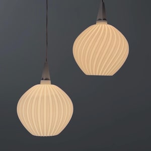 Könnte beinhalten: Zwei Pendelleuchten mit cremefarbenen, gerippten, kugelförmigen Schirmen. Die Schirme haben ein Spiraldesign und sind an dünnen Schnüren von der Decke abgehängt. Die Leuchten haben ein modernes Design vor einem dunkelgrauen Hintergrund.