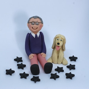May include: A figurine wearing a purple sweater and glasses sits next to a light brown dog figurine. Both figurines are surrounded by black star-shaped decorations.