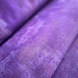 May include: Purple fabric with a textured, slightly distressed look. The fabric has a subtle ombre effect, with lighter shades of purple at the edges and darker shades in the center.