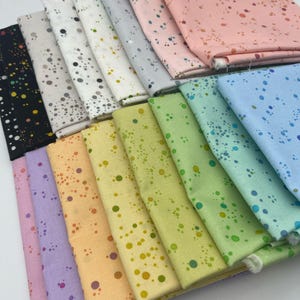 Könnte beinhalten: Ein Stapel von 18 Stoffquadraten mit einem gesprenkelten Muster in verschiedenen Farben, darunter Lila, Orange, Gelb, Grün, Blau und Rosa.