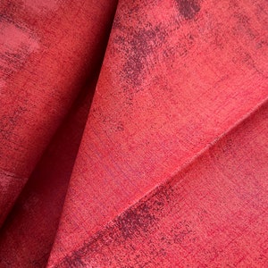 May include: Close-up of a red fabric with a textured, slightly distressed surface. The fabric has a subtle sheen and a slightly wrinkled appearance.