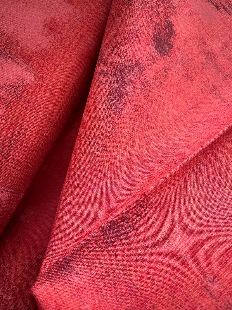 May include: Close-up of a red fabric with a textured, slightly distressed surface. The fabric has a subtle sheen and a slightly wrinkled appearance.