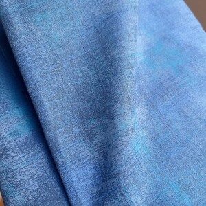 May include: Close-up of blue fabric with a textured appearance. The fabric has a mix of light and dark blue hues, with subtle streaks of turquoise. The material appears to be soft and flowing, suggesting it could be used for clothing or home decor.