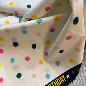 Könnte beinhalten: Weißer Stoff mit bunten Tupfen in Rosa, Gelb, Türkis und Beige. Ein marineblauer Rand mit dem Wort "BIRTHDAY" in Gelb und weißen Sternen.