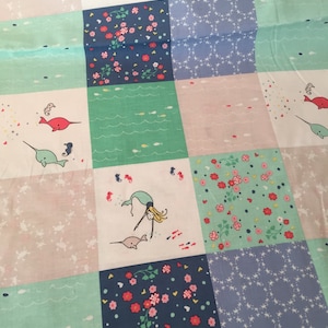 Könnte beinhalten: Ein Patchwork-Stoff mit einem sich wiederholenden Muster aus Meerjungfrauen, Narwalen, Seepferdchen und Blumen. Der Stoff ist in den Farben Rosa, Blau, Grün und Weiß gehalten.