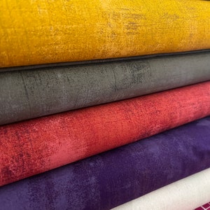 May include: A stack of six fabric rolls in various colors, including beige, yellow, gray, red, purple, and beige. The fabric has a textured, distressed look.