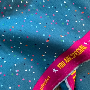 Könnte beinhalten: Türkisfarbener Stoff mit einem Streumuster aus Punkten in verschiedenen Farben. Ein magentafarbenes Band mit dem Text "YOU ARE SPECIAL" und dem Markennamen "wattsalot" ist sichtbar.